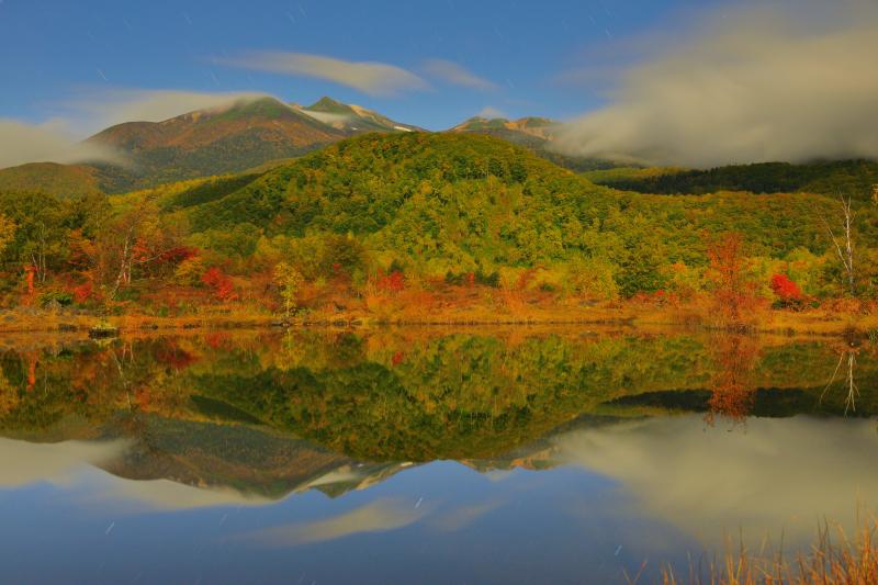 [ 月光乗鞍 紅葉シンメトリー ]  月明かりに照らされたまいめの池。乗鞍岳を流れる雲、空を舞う星たちが穏やかな水面に映り込んでいました。