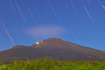 月明かりに照らされた真夏の富士山。山小屋の灯りと登山客のヘッドランプが見えます。空には星が輝いていました。