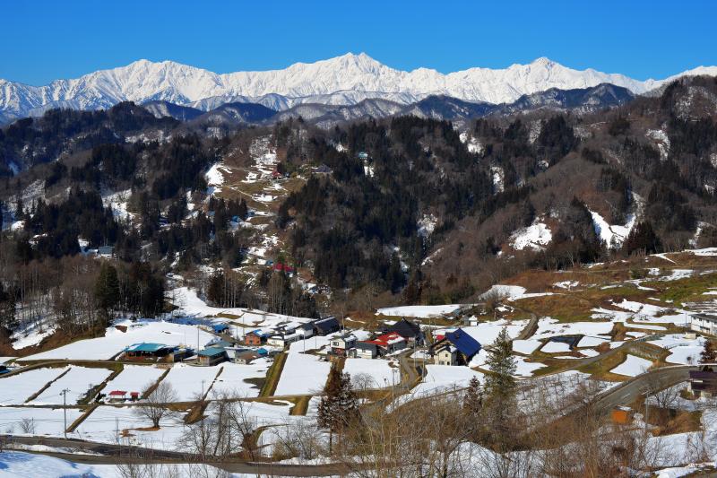 [ 冬晴れ ]  厳冬期の北アルプス「仁科三山」左から爺ヶ岳・鹿島槍ヶ岳・五竜岳。冬型の気圧配置がゆるみ好天が続くと道路の雪は消え乾燥路面に。朝・晩・日陰はスリップ注意。